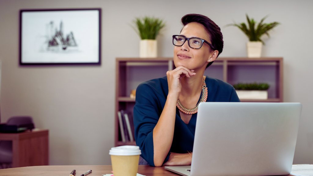 Artfully Media - Recruitment Advertising Made Simple Improve job advertising ROI without additional spend - Think differently when it comes to recruitment, lady sat a desk with a coffee and a laptop. The lady is gazing up deep in thought.